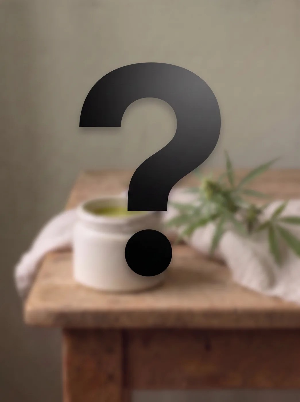 Großes Fragezeichen über einem Tiegel mit grüner CBD Creme auf einem Holztisch, daneben ein Hanfzweig.
