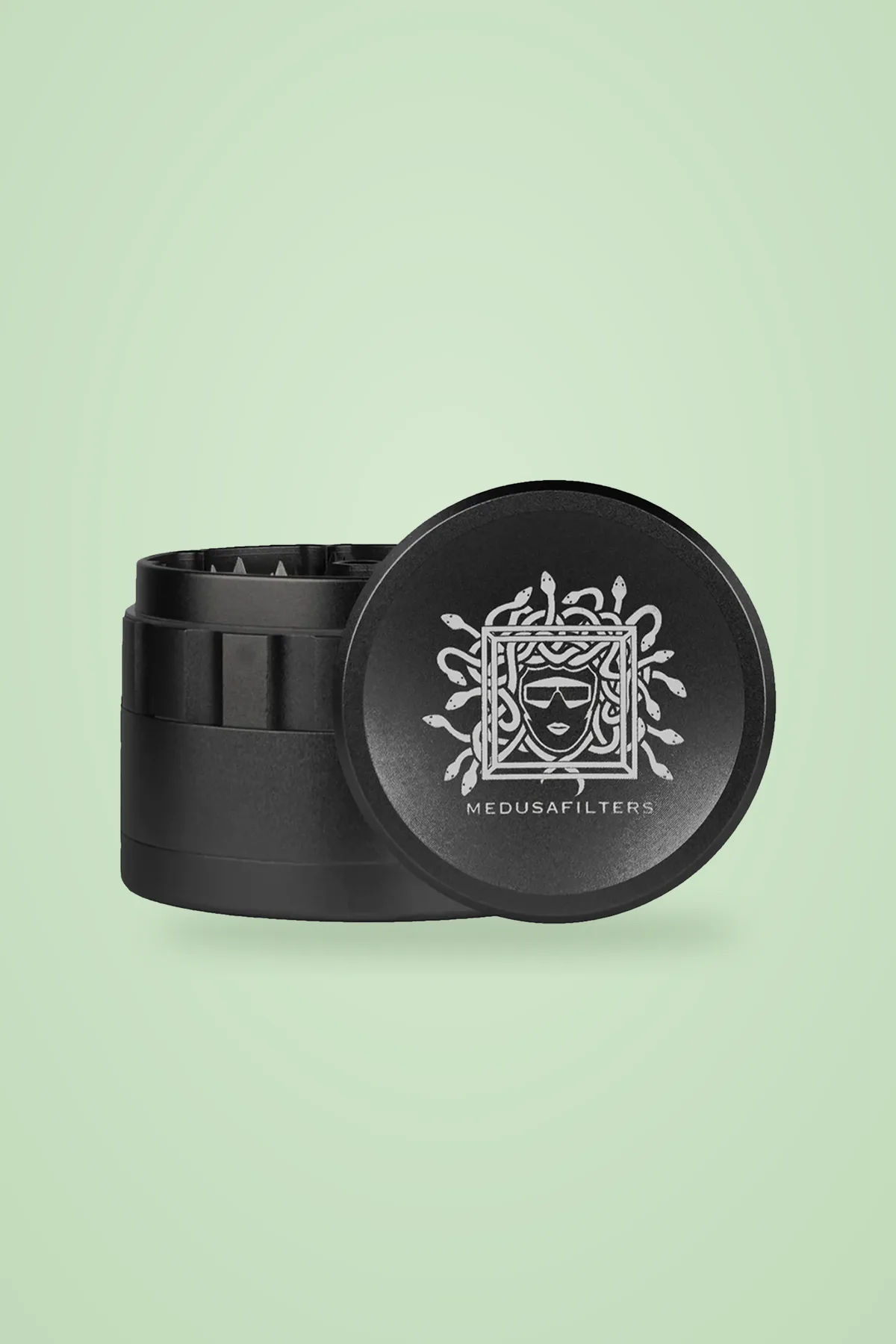 Schwarzer Medusafilters Grinder aus Aluminium, 4-teilig mit 63,5 mm, geöffnet vor grünem Hintergrund.